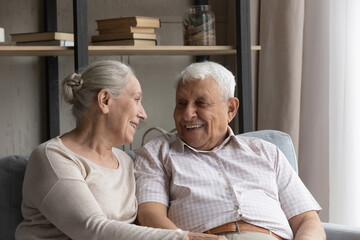 Happy laughing candid older mature married family couple enjoying pleasant conversation, resting together on cozy couch. Loving smiling senior retired man and woman talking discussing life news.