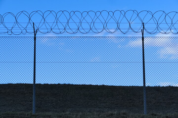 Spulen von Stacheldraht auf einem Maschendrahtzaun  hinter blauem Himmel