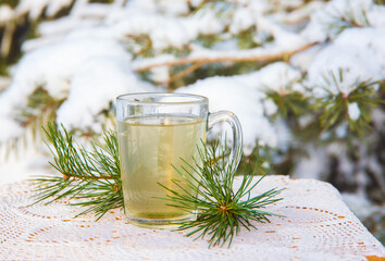 Hot pine tree needle tea infusion in transparent glass tea cup on table. Snowy pine tree on...