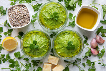 Fresh homemade parsley and sunflower seeds green pesto style dip in glass jars with ingredients, top view.