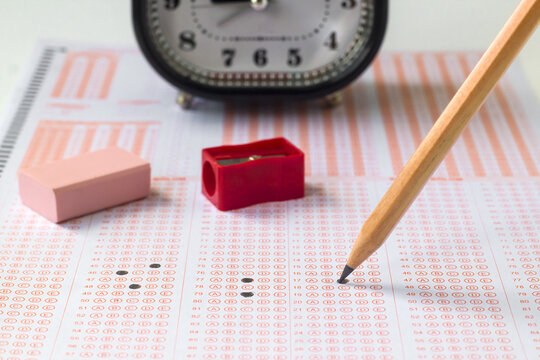 Alarm clock,wooden pencil and rubber on filled exam sheet,conceptual image of education qualifying test exam.