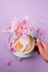 Female hands holding a cup of coffee. Blouse with romantic pink background and rose petals.