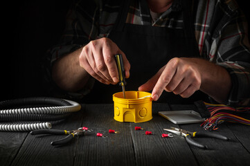Close-up of hands of a master electrician during work. Installing a cable or wire to yellow junction box. Free advertising space