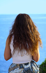 Fototapeta na wymiar The back of a girl with long brown hair looking towards the sea horizon in front of her