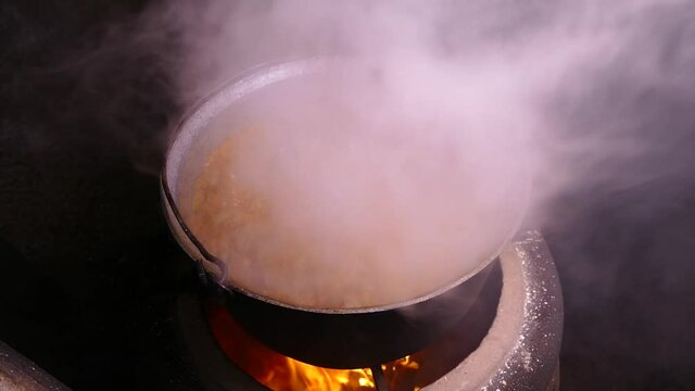 Goulash is prepared with seasoning and meat. Steam from a hot dish. Kitchen in a cauldron. Stir with a kitchen spatula. Campfire food.
