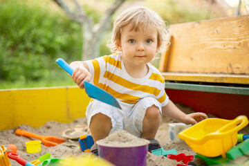 A little boy playing in the sandbox at the playground outdoors. Toddler playing with sand molds and...