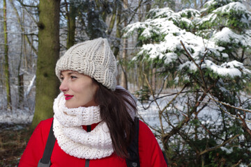 Woman walking in the woods in winter outdoors. Girl in red clothes and white hat hiking in snowy forest. Frosty sunny day in December. Female lifestyle portrait