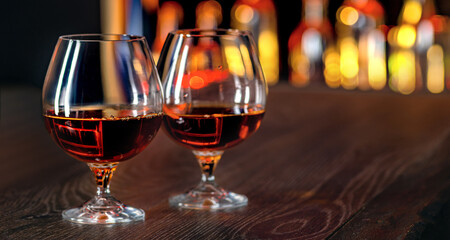 Brandy glass on the bar counter. Alcoholic beverage, cognac, whiskey, port, brandy, rum, scotch, bourbon. Vintage wooden table with drinks in front of showcases with bottles in the dark