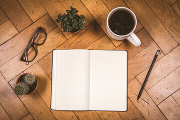 Blank checkered notebook, pencil, glasses, cup of coffee, plants on wooden background, writing concept, top view