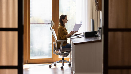 Serious home distance employee doing paperwork at table, reviewing financial paper reports at...