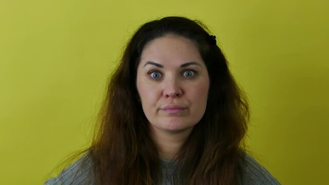 Woman in a state of doubt. Beautiful woman in gray sweater with long hair on yellow background in a state of reproach and bewilderment.