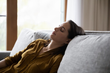 Tired millennial young woman sleeping in sitting position on couch, leaning on back with closed...