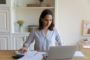 Focused satisfied millennial homeowner woman using financial banking online application on laptop...
