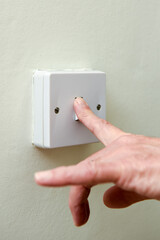 Person turning off light switch to save on energy bills and waste of electricity