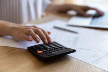 Hand of African finance professional woman using calculator, payment app on laptop, calculating project cost, paying bills, taxes, counting mortgage fees on Internet. Close up of workplace table