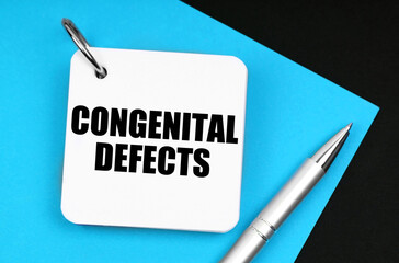 On the black surface lies blue paper, a pen and a notebook with the inscription - congenital defects
