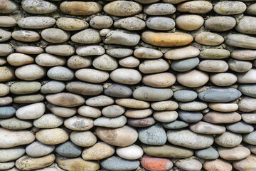 Full frame image of wall made of gray rounded pebbles. Close-up front view. Natural wallpaper, background or texture