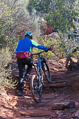 A mountain biker dismounts to ascend a steep part of the Peccary Trail in Sedona, Arizona.