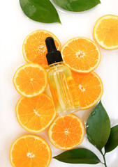 Beauty concept of Vitamin C serum in cosmetic bottle with dropper and slices of orange fruit on white background.