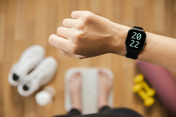 Looking at fitness tracker with 2022 number while standing on scales, first person view. Smart watch on female hand, point of view, concept of new year and new beginnings, goals for the year.