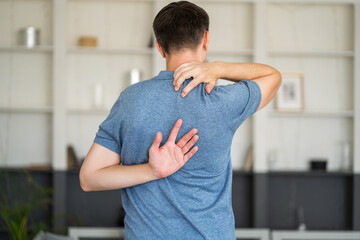Pain between the shoulder blades, man suffering from backache at home