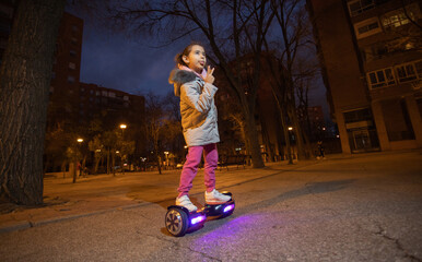 Sport and Mental Health series. Hispanic American girl enjoying her electric scooter on a street in her neighborhood on a night walk in autumn concept: freedom, joy, happiness, urban culture
