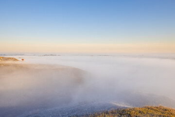 Autumn landscape in the early morning. Fog-covered expanses through which the first rays of the rising sun pass. Trees and hills in the fog. Dawn on a cold autumn morning.