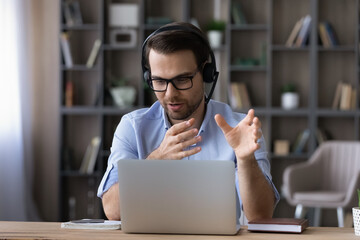 Businessman in glasses and headset talking, making video call looking at laptop screen, chatting...
