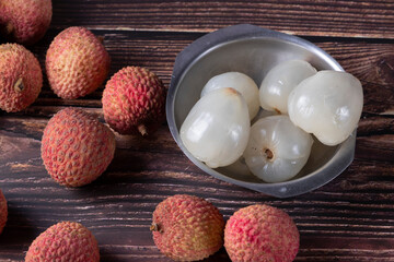 Tasty Lychee (Litchi chinensis, scientific name in Latin), on a wooden table with some without shells, served over stainless steel bowl. Selective focus.