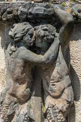 Fototapeta na wymiar Two stone figures are kissing. Embracing male and female half figures carrying a ledge in a baroque garden