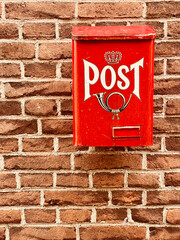 Traditional old bright red metal post box with word and picture of horn on front attached to the...