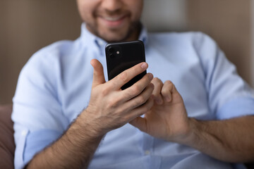 Cropped close up smiling man using smartphone in hands, typing and looking at screen, writing message, chatting online in social networks, browsing mobile device apps, playing game or shopping