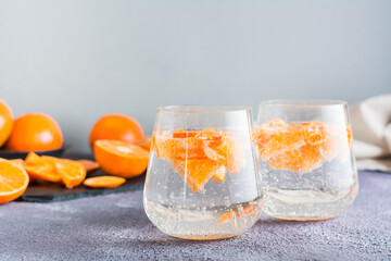 Refreshing drink mineral water with pieces of tangerine in glasses and ripe fruits next to on the table. Detox food