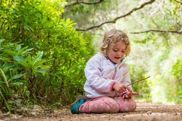 Cute blonde girl sitting on forest trail enjoying the nature and posing.