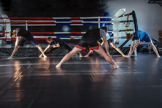 The trainer conducts a training session with a group of teenage boxers. Children repeat stretching exercises after the trainer in the background of the ring. - Powered by Adobe