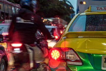 A motorbike overtakes a queue of cars in a traffic jam. Evening traffic on the city streets, Bangkok, Thailand.