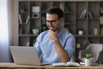 Fototapeta na wymiar Excited successful businessman in glasses looking at laptop screen, reading good news in message or email, happy laughing young man freelancer or student received unexpected offer, notification