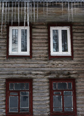 Long icicles hang from the roof of a wooden house to the very windows.