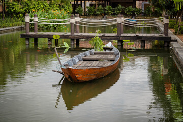 Fototapeta na wymiar Wooden boat on the pond near the pier in a tropical garden in Danang, Vietnam