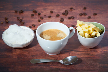 Bulletproof coffee in a white cup. Coconut oil, butter and coffee beans can be seen. Spoon is in front of the cup. Close up. Bulletproof coffee is also part of the ketogenic diet.