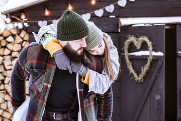 couple of young woman and man having fun in courtyard of decorated suburban house in winter, concept of Christmas and New Year vacation on farm, family love and support, Valentines Day celebration