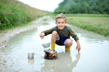 A little boy in rubber boots is playing in a puddle after the rain.