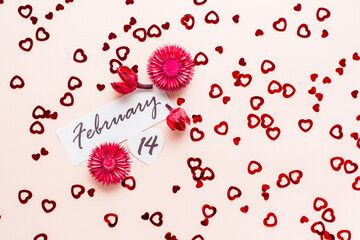 Valentine's Day. Date of February 14 and dry flowers on a pink background strewn with hearts. Top view