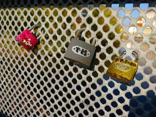 Three love padlocks fixed on the bridge's metal fence. One is pink, one gray, and another on is gold.