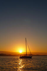 Silhouette of a sailboat on the Adriatic Sea with the sunset, mountains and clear, blue sky in the background. Zadar - Croatia