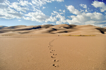 The small figure of a man walks in the distance across a desert towards towering sand dunes leaving...
