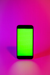 Mobile phone with green screen, smartphone mock up. Neon illumination. Pink and purple color. Flat screen modern smartphone