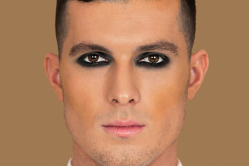 Closeup portrait of a young White man with short brown hair, light makeup and dark eyeshadow...