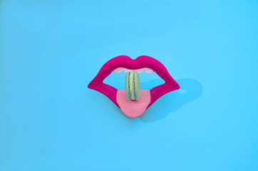 Bright magenta lips with a lime green French macaron on a pink tongue. Blue background. Provocative Valentine's concept for banner. Sexy design for cosmetics, lipstick of fashion commercial.
