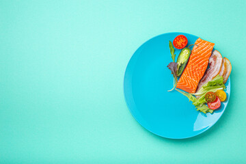 Intermittent fasting low carb hight fats diet concept flat lay, healthy food salmon fish, bacon meat, vegetables and salad on blue plate and blue background top view 
